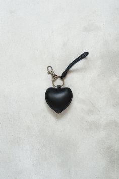 a black heart shaped keychain hanging from a cord on a white surface,