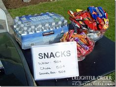 snacks and water are on the table for sale at an outdoor event in front of a house