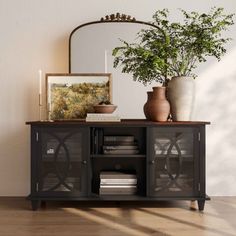 a black cabinet with books and vases sitting on top of it next to a mirror