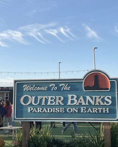 a sign that says welcome to the outer banks paradise on earth with people standing around it