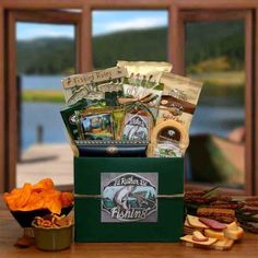 a green box filled with snacks on top of a wooden table next to a lake