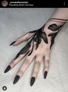 a woman's hand with black nail polishes and leaves on the left palm