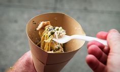 a hand holding a paper cup filled with food and a white plastic spoon in it