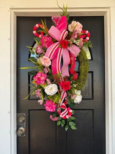 a wreath with pink and white flowers is hanging on the front door's black door