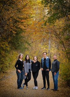 a group of people standing on a dirt road surrounded by trees in the fall colors