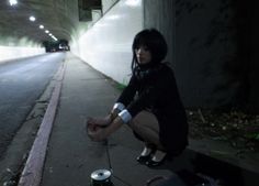 a woman kneeling down next to a can on the side of a road at night