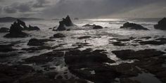 the sun shines through clouds over some rocks in the water on a cloudy day