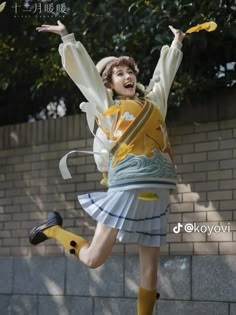 a woman in a yellow shirt and white skirt jumping up into the air with her arms outstretched