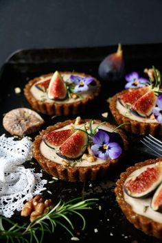 several small tarts with figs and flowers on them, next to a fork