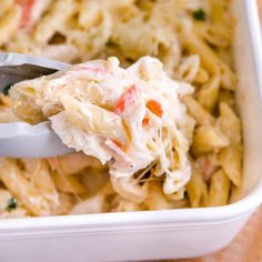 a spoon full of pasta with chicken and carrots on it is being lifted from the casserole dish