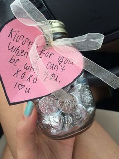 a hand holding a jar with candy in it and a heart shaped tag attached to the top