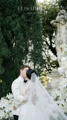 a bride and groom are kissing in front of white flowers at their wedding day,