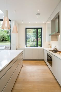 an empty kitchen with white cabinets and wood flooring in front of a large window