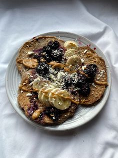 a white plate topped with pancakes covered in bananas and blueberry compote toppings