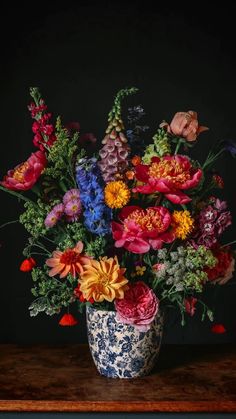 a blue and white vase filled with lots of colorful flowers on top of a wooden table