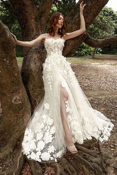 a woman standing in front of a tree wearing a white dress with flowers on it