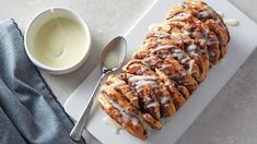 a white plate topped with cinnamon rolls covered in icing next to a cup of milk