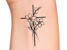 a cross and flowers tattoo on the back of a woman's leg, with black ink