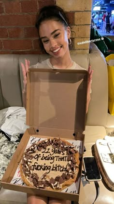 a woman holding up a birthday cake in a box