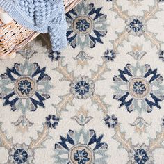 an area rug with blue and white flowers on it, next to a basket full of blankets