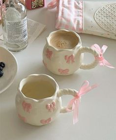 two coffee mugs with pink bows on them