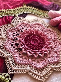 crocheted doily and yarns are laying on the table top, including one pink flower