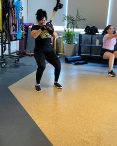 two women in a gym doing exercises with baseball bats on the floor while another woman watches