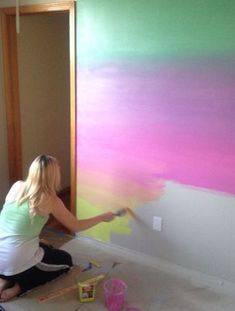 a woman is painting a wall with pink and green colors