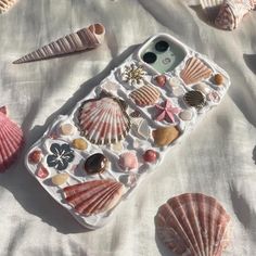 an iphone case with seashells and shells on the cover is laying on a bed