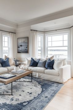 a living room filled with furniture and windows covered in white curtains on top of a blue rug