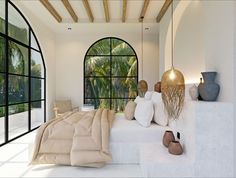 a bedroom with white walls and flooring next to a large arched window that overlooks palm trees