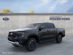 a black truck is parked in front of a power ford sign and wall with the company's logo on it