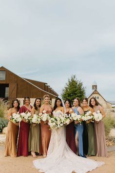 a group of women standing next to each other in front of a barn holding bouquets