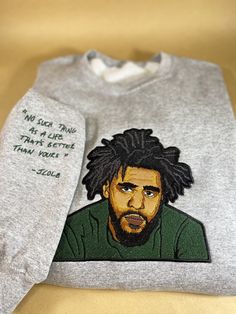 "Wrap yourself in comfort and style with this custom embroidered sweatshirt featuring a detailed portrait of the legendary rapper J. Cole on the chest, and his iconic lyric \"No such thing as a life that's better than yours\" stitched on the right sleeve. The sweatshirt's design captures the essence of J. Cole's artistry and delivers a powerful message of self-worth and positivity. 🎨 **Customization Options You have the freedom to choose the color of J. Cole's shirt on the portrait as well as t Winter Sweater With Custom Embroidery For Streetwear, J Cole Hoodie, J Cole T Shirt, Cozy Love, Detailed Portrait, Unique Wardrobe, Embroidered Portrait, Relaxed Outfit, J Cole