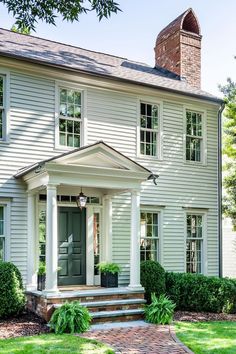 a white house with green doors and steps leading up to the front door is surrounded by greenery