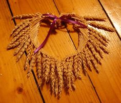 a heart shaped wreath made out of wheat on a wooden floor with purple ribbon around it