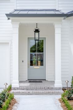 the front door of a white house with a light fixture hanging from it's side