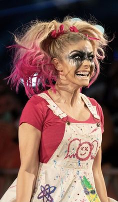 a woman with pink hair and makeup is walking down the catwalk wearing an apron