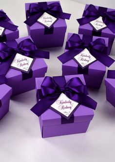 many purple boxes with ribbons and name tags are arranged on a white surface, each containing a bow