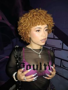 a woman with curly hair wearing a sheer top and holding her hands in her pockets