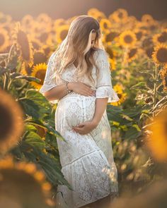 a pregnant woman standing in a field of sunflowers with her hands on her stomach