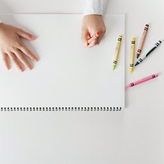 a child's hand on top of a white sheet of paper with crayons next to it