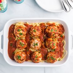 spaghetti and meatballs with sauce in a white casserole dish on a table