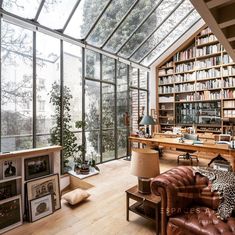 a living room filled with lots of books and furniture next to a large glass window