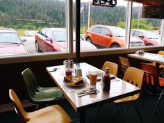 there are many tables and chairs in this restaurant with cars out the window behind them