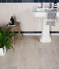 a white sink sitting next to a green plant on top of a wooden stool in a bathroom