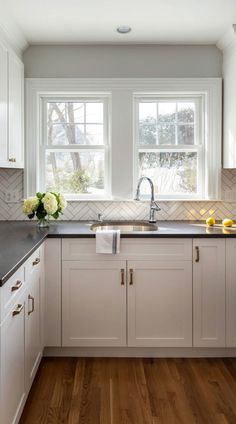 a kitchen with white cabinets and black counter tops next to a window filled with flowers