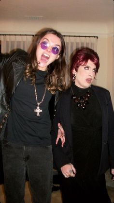 two women standing next to each other in front of a window wearing purple glasses and black clothing