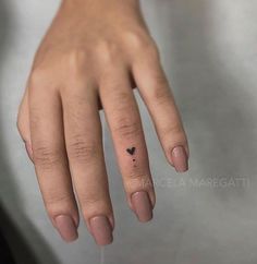 a woman's hand with a tiny black heart tattoo on her left ring finger