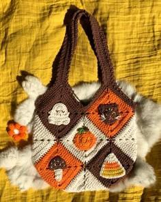 a crocheted handbag with cats and pumpkins on the front is laying on a yellow blanket